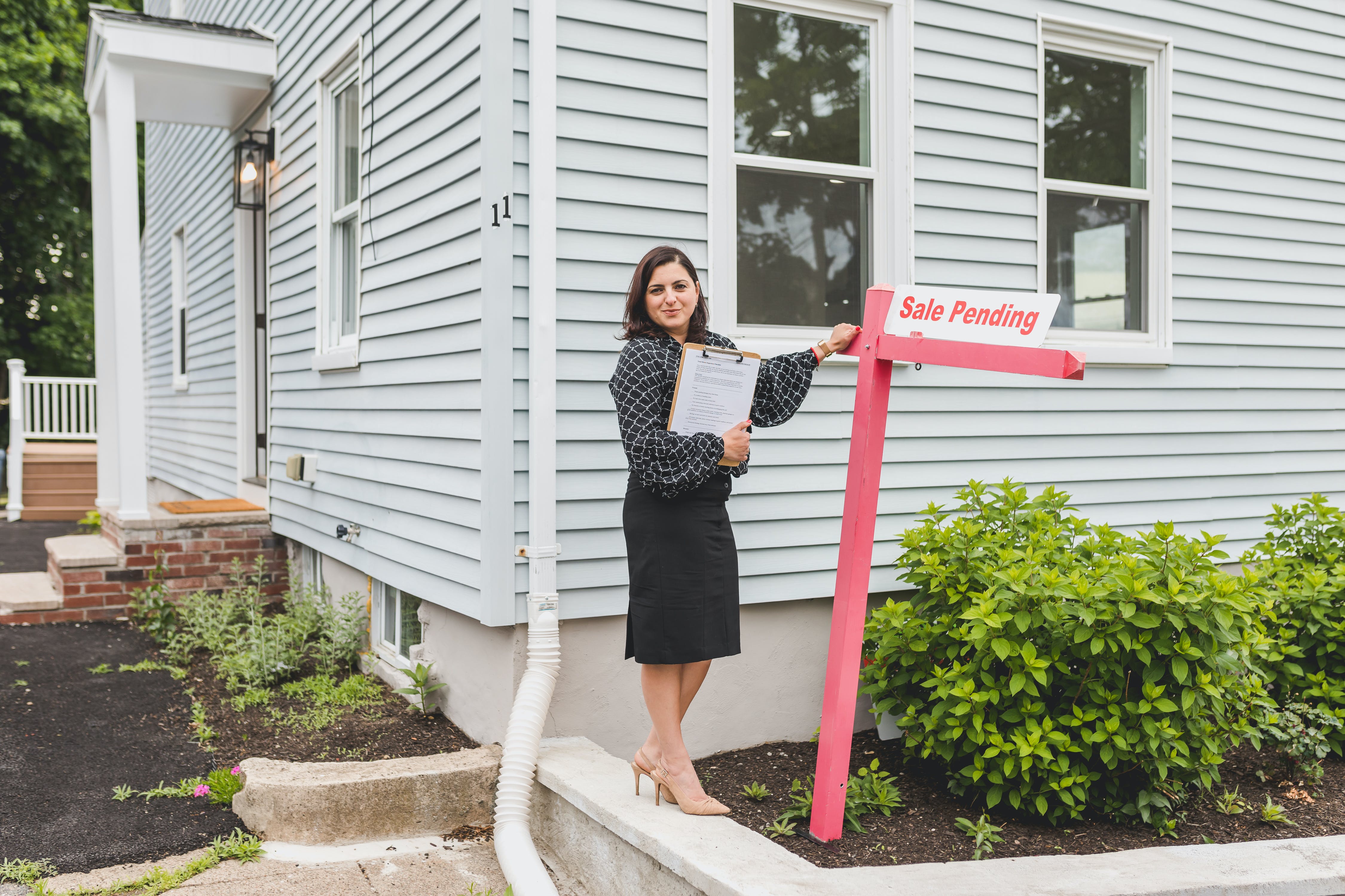 Real estate agent in front of house with for sale sign